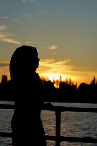 Silhouette woman standing by lake against sky during sunset