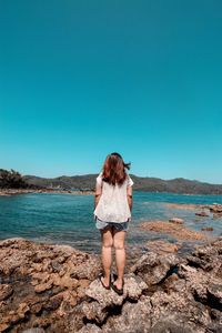 Rear view of woman standing on beach against clear blue sky