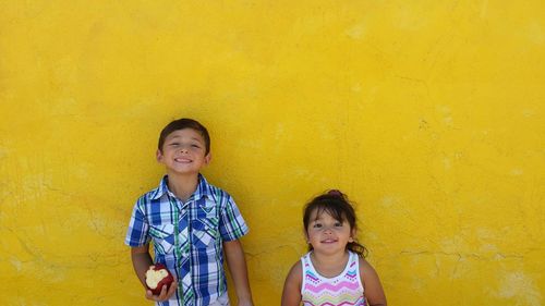 Cute siblings standing against yellow wall