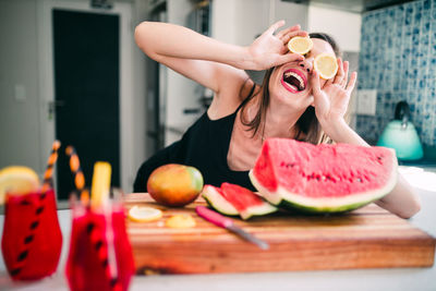 Young woman with fruits laughing on table at home