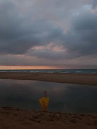 Man sitting on beach against sky during sunset