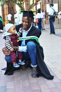 Father wearing graduation gown with toddler son at university