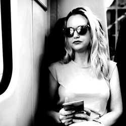 Mid adult woman wearing sunglasses using smart phone while sitting in train