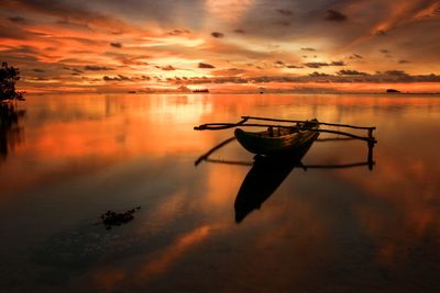 Silhouette boat moored in sea against sky during sunset
