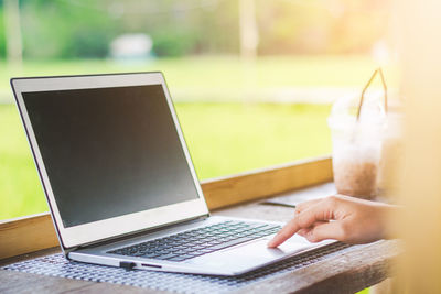 Cropped hands of woman using laptop on wooden table against landscape