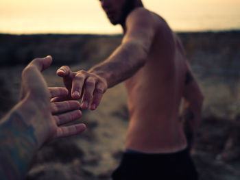 Cropped image of woman holding shirtless man hand at beach