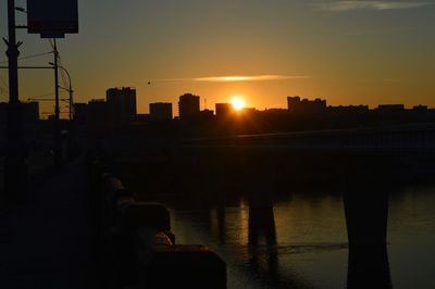 Silhouette city by river against sky during sunset