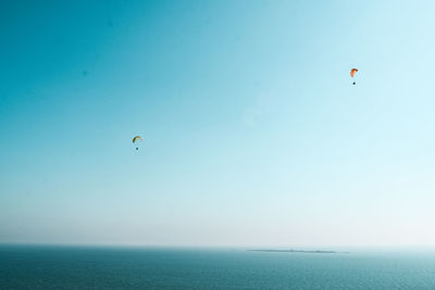 Scenic view of sea against clear sky with paragliders and islands