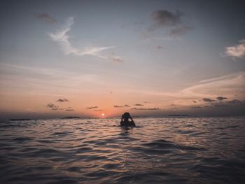 Silhouette of man in sea against sky during sunset