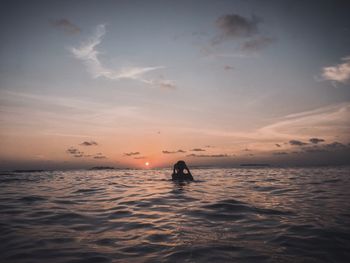 Silhouette man in sea against sky during sunset