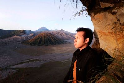 Portrait of young man on rock against sky