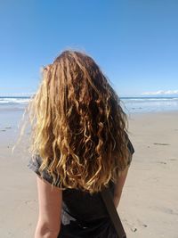 Rear view of woman at beach against sky