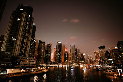 Illuminated buildings by river against sky in city at night