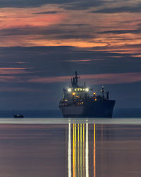 Illuminated ship sailing on sea against sky during sunset