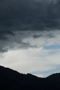 Low angle view of storm clouds over silhouette mountain