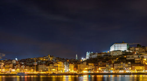 Illuminated buildings by sea against sky at night