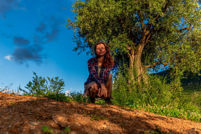 Portrait of young woman sitting on plant against trees