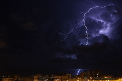 Lightning over illuminated cityscape against dramatic sky at night