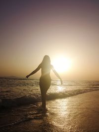 Silhouette woman standing at beach against sky during sunset