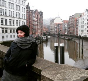 Portrait of smiling woman leaning on bridge over canal amidst buildings during winter