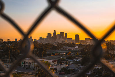 Cityscape seen through chainlink fence during sunset