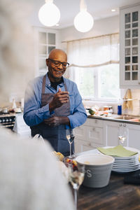 Smiling bald senior man rolling up sleeves before preparing dinner in kitchen at home