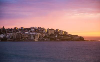 Sea by buildings against sky during sunset