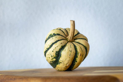 A cream and green mini pumpkin standing up on a wooden chopping board