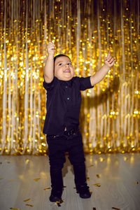 Boy in black clothes at christmas standing in a room on a background of gold tinsel on the wall