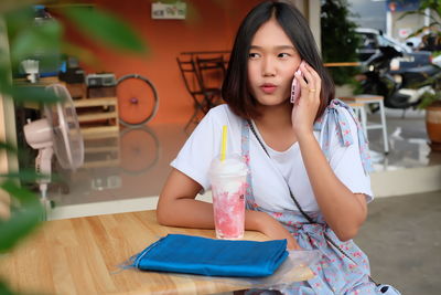 Young woman talking on smart phone while sitting at sidewalk cafe