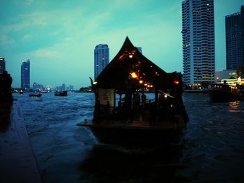 Illuminated city by river against sky