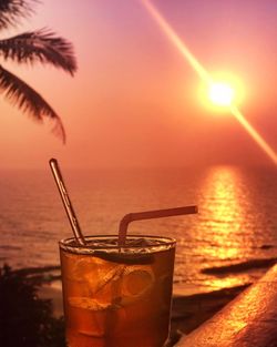 Close-up of drink on beach against sky during sunset