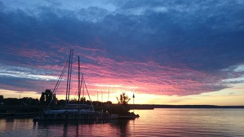 Boat moored on lake against cloudy sky during sunset