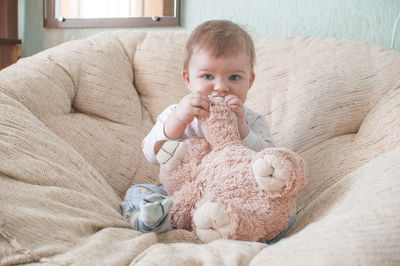 Portrait of baby girl biting teddy bear on sofa at home