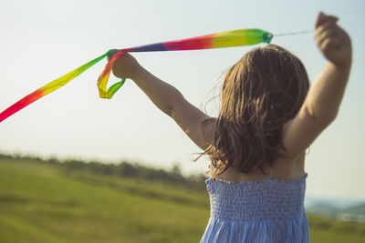 Rear view of girl with arms raised holding toy against sky