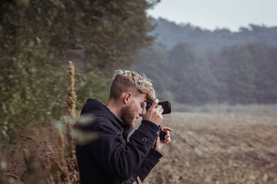 Side view of man photographing while standing on field