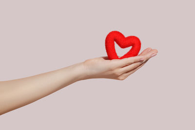 Cropped hand holding red heart shape against white background