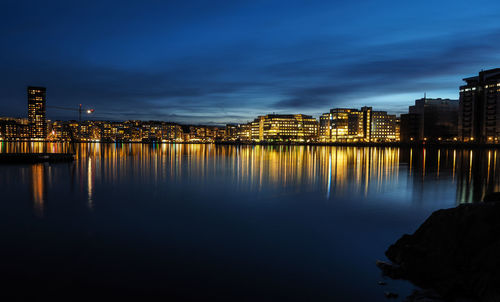 Illuminated buildings by river against sky at night