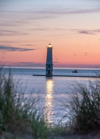 Lighthouse by sea against sky during sunset