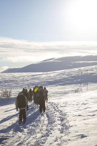 Rear view of people splitboarding on snow covered landscape