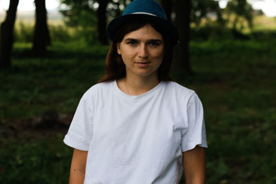 Portrait of a tired young woman with brown hair wearing a hat outdoors. green nature background. 
