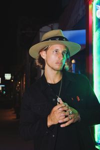 Young man wearing hat standing at night