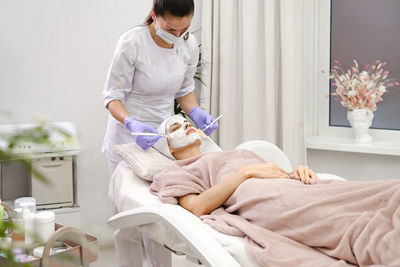 Cosmetologist apply skin mask with brush, care and treatment procedure in modern aesthetic clinic