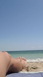 Midsection of woman relaxing on beach against clear sky