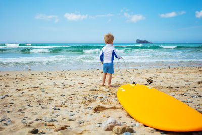 Rear view of boy standing at beach against sky