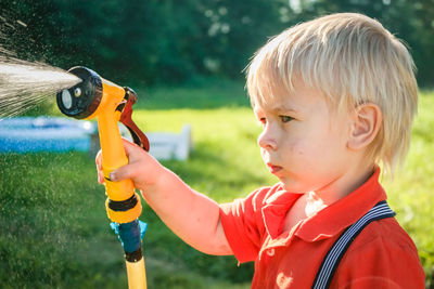 Cute little boy watering flowers in the garden. young child splashing water from garden water hose.