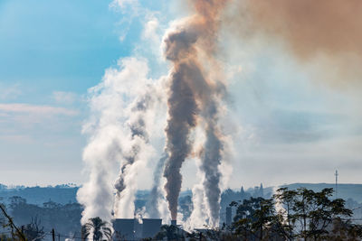 Smoke emitting from factory against cloudy sky