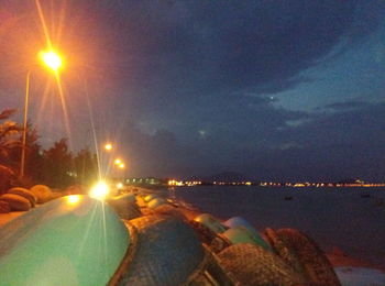 Close-up of illuminated city at beach against sky during sunset