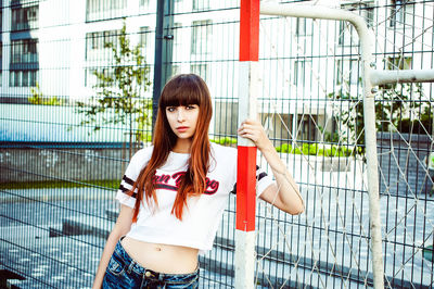 Portrait of young woman standing by soccer goal post