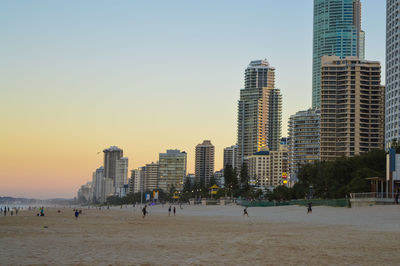 People on beach by city against clear sky